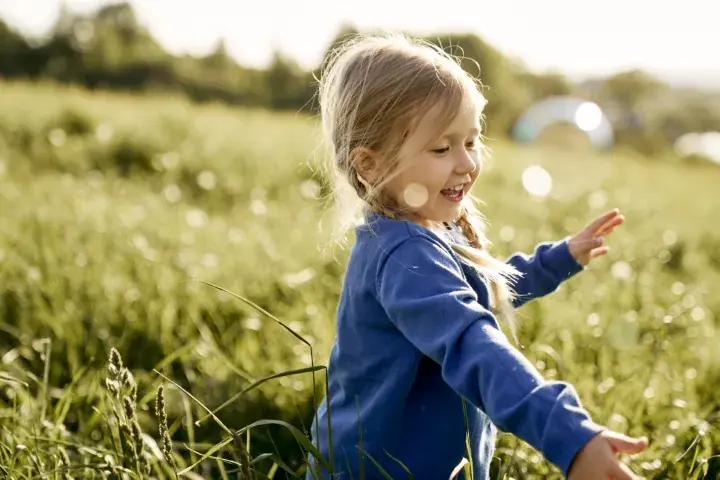 Joyful young girl playing in a sunlit field of tall grass