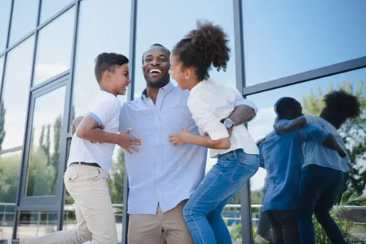 Happy father embracing his son and daughter outside a modern building with reflection of their hug